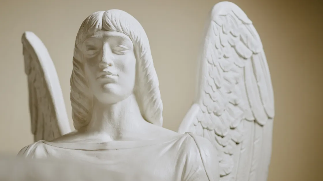 Escultura de anjo em gesso branco, close-up do rosto e das asas, dentro de uma igreja católica