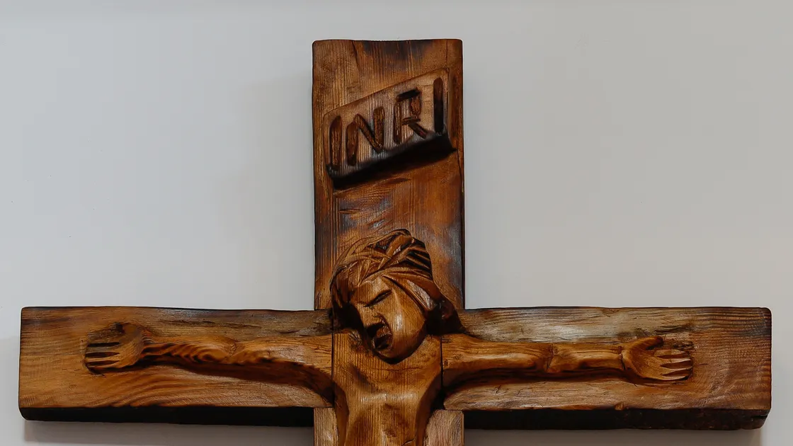 Crucifixo de madeira entalhada, com a inscrição INRI no topo, pendurado numa parede clara de igreja