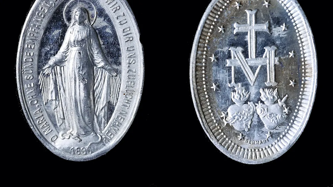 As duas faces de uma Medalha Milagrosa antiga sobre fundo preto: a frente com Nossa Senhora de braços abertos e a data 1830, o verso com a letra M coroada por uma cruz, doze estrelas e os dois Sagrados Corações.
