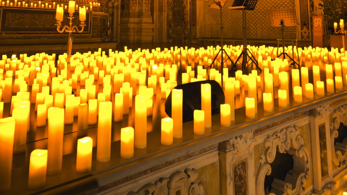 Interior de igreja barroca com centenas de velas acesas diante do altar, talha dourada e um quadro antigo ao fundo.