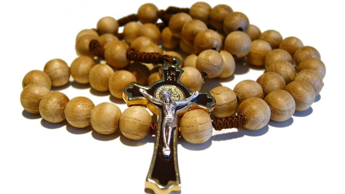 Terço de contas de madeira clara enrolado, com crucifixo esmaltado dourado e prateado, sobre fundo branco